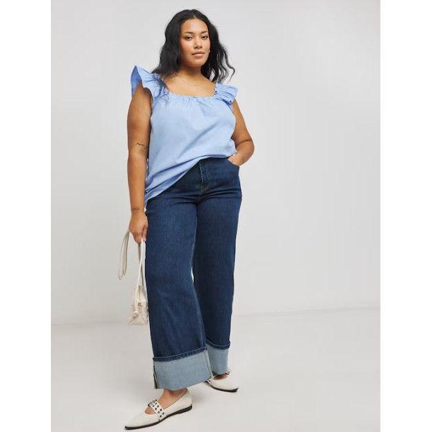 Woman wearing a light blue top and dark blue jeans against a plain background