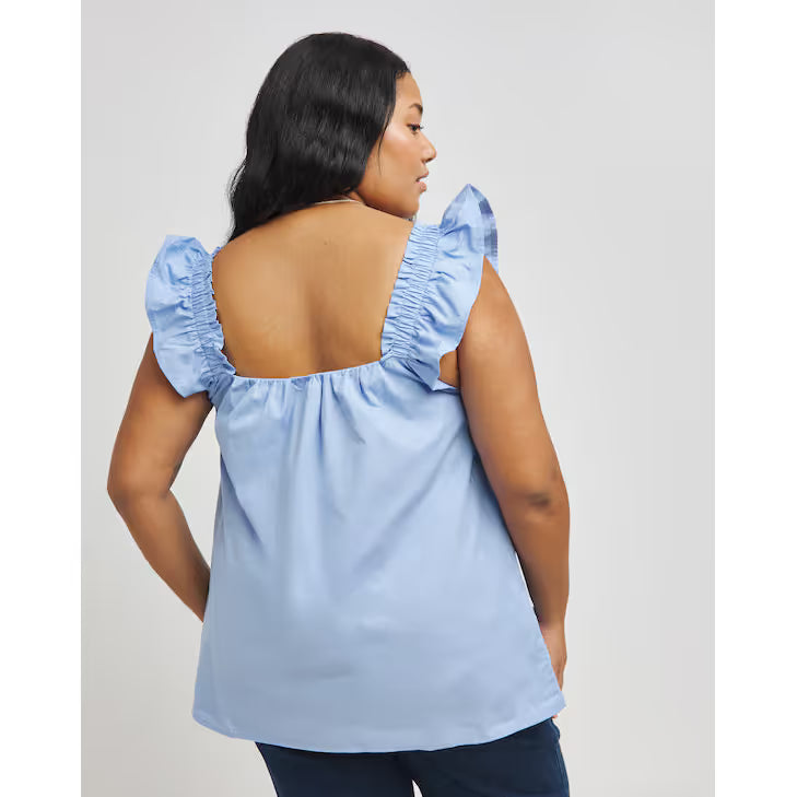 Woman wearing a light blue blouse with ruffled shoulders against a plain background