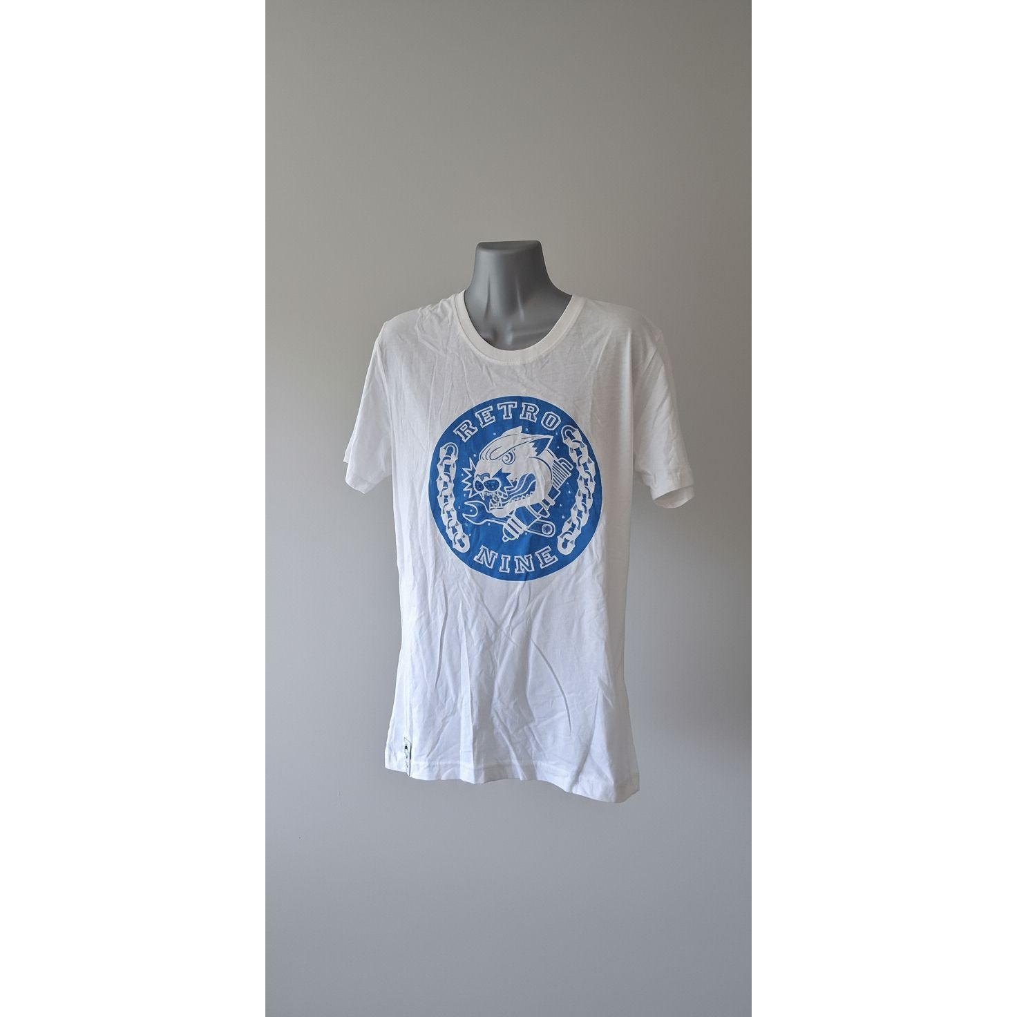 White t-shirt with a blue logo on a mannequin against a gray tiled wall.