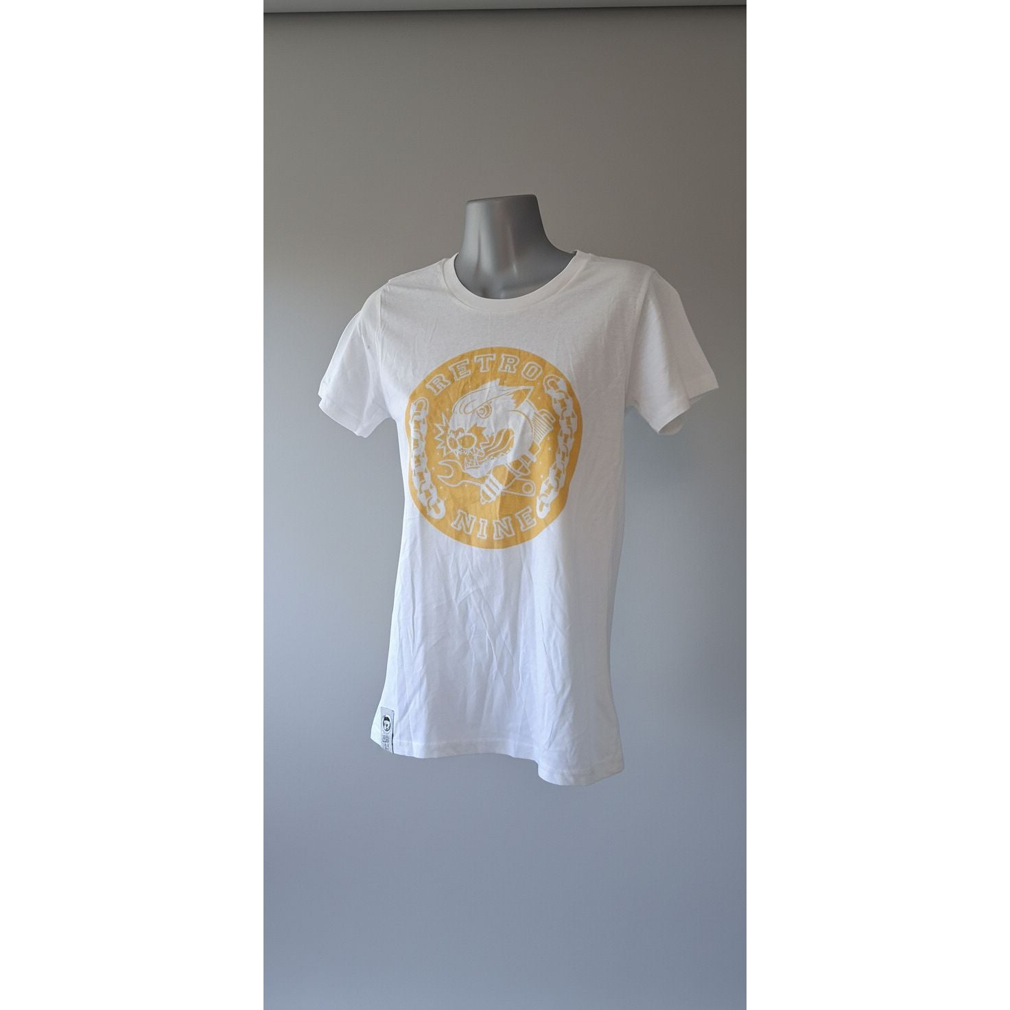 White t-shirt with yellow logo on a mannequin against a tiled wall.