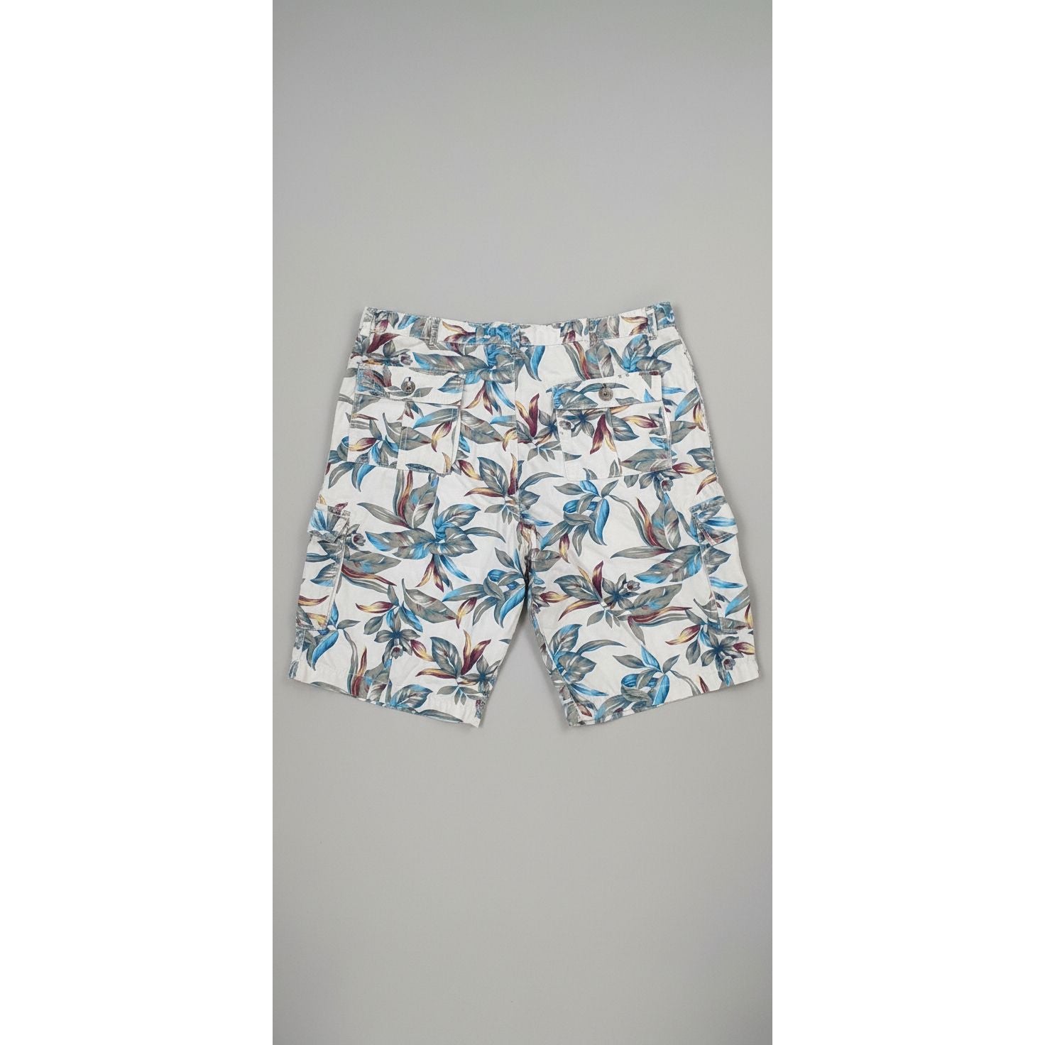 Floral-patterned shorts on a textured floor with a person wearing white socks and gray shoes.