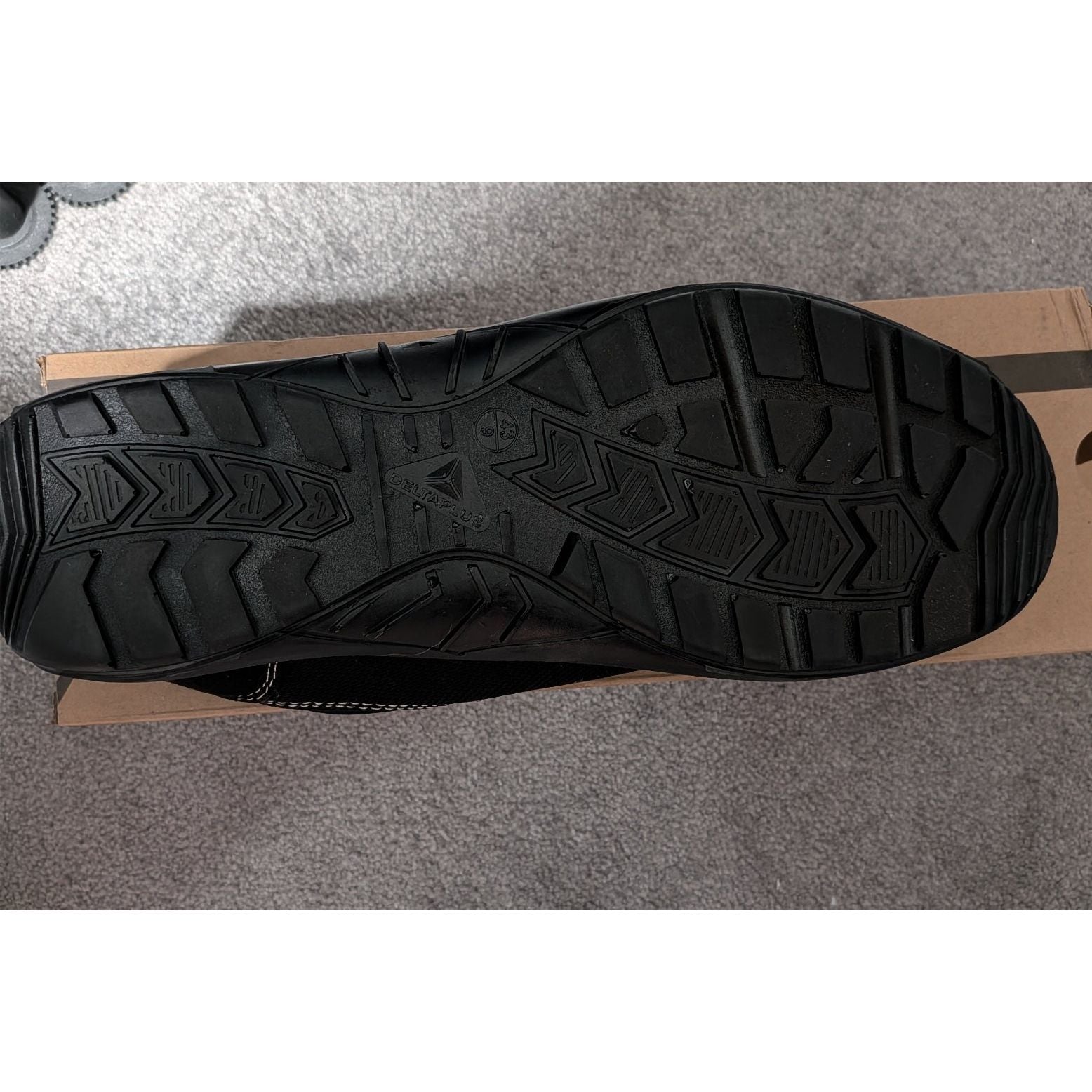 Black sole of a shoe on a cardboard box with a gray floor background
