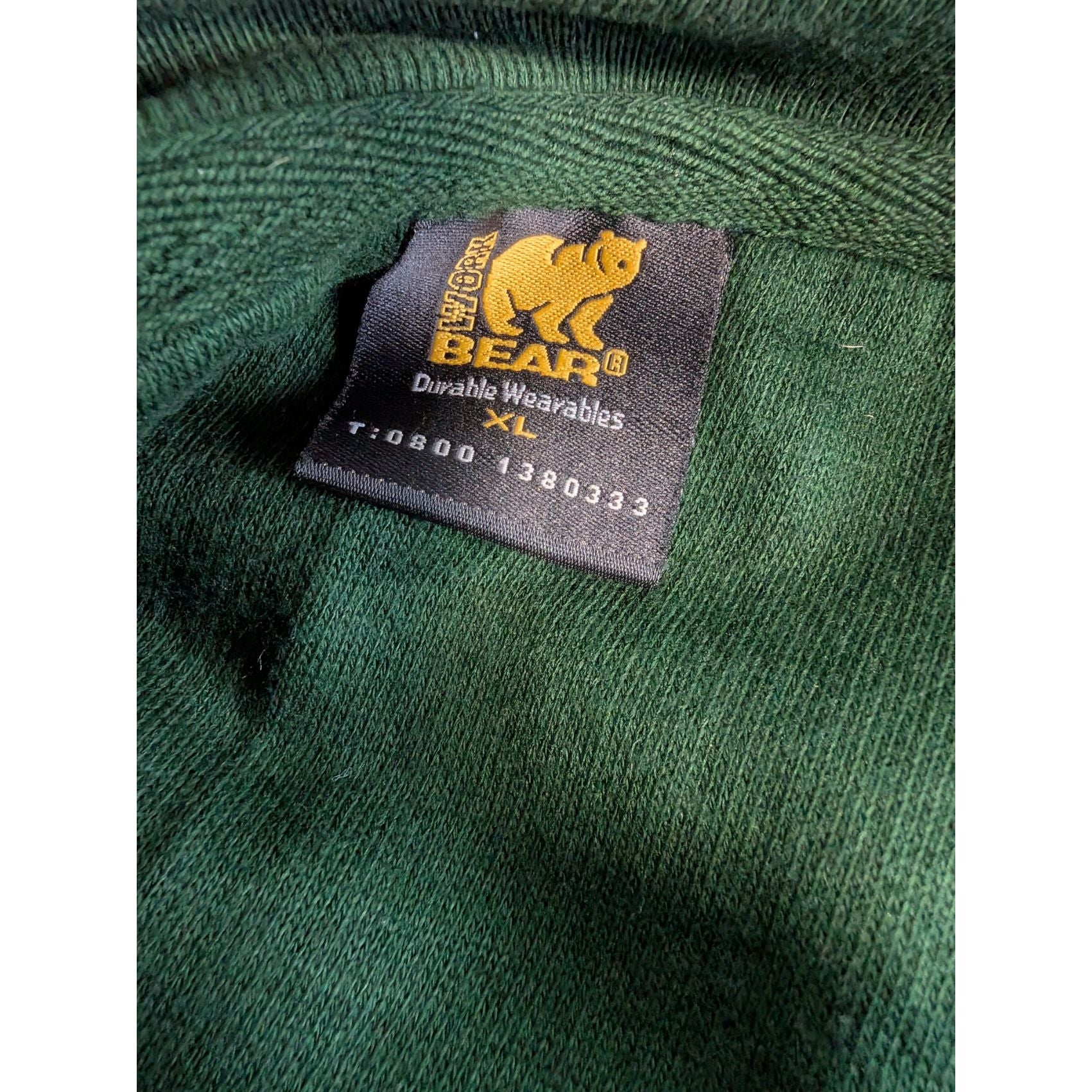 Close-up of a label on a green garment with a bear logo.