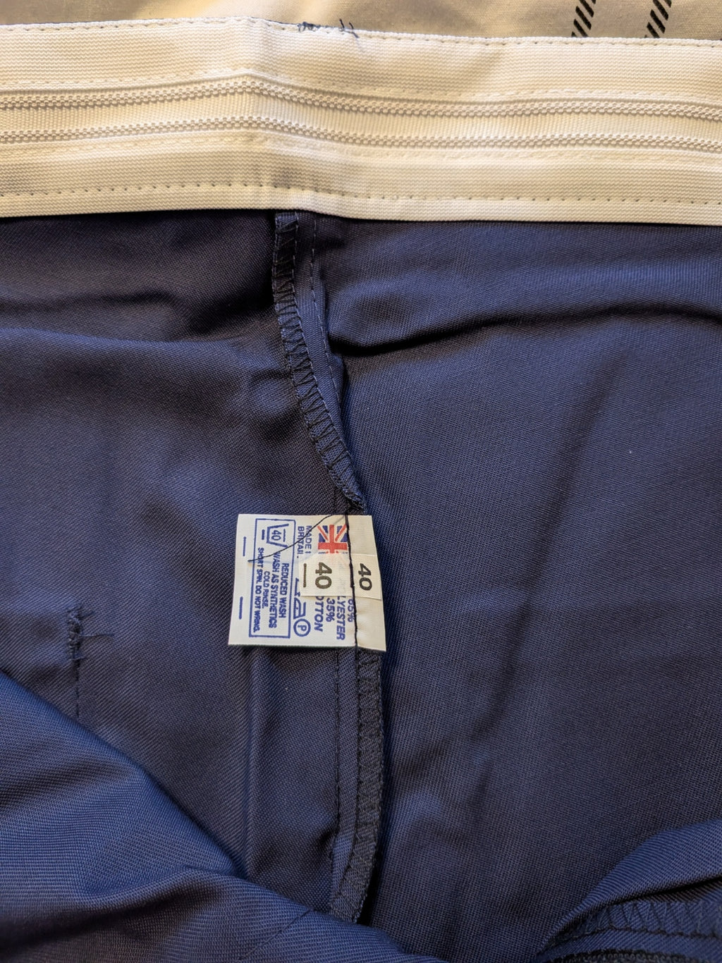 Close-up of the waistband and inner label of navy blue pants, showing a white elastic waistband and a sewn-on size 49 tag.