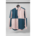 A long-sleeve colorblock shirt with a pink collar and button placket, featuring large blocks of dark teal blue and light pink, hanging on a black hanger against a wooden door.