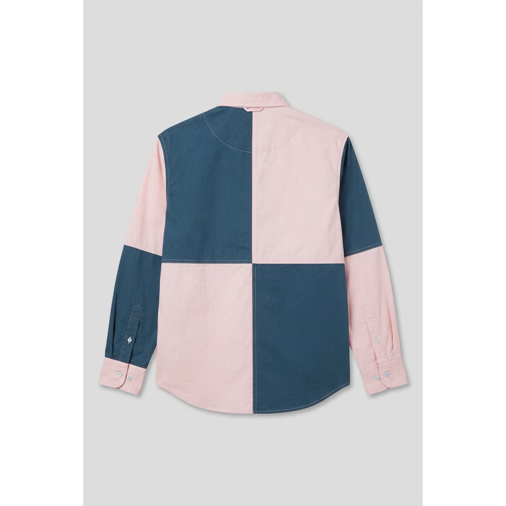 A long-sleeve color-block shirt with a large checkered pattern in teal blue and light pink, shown hanging on a wooden door.
