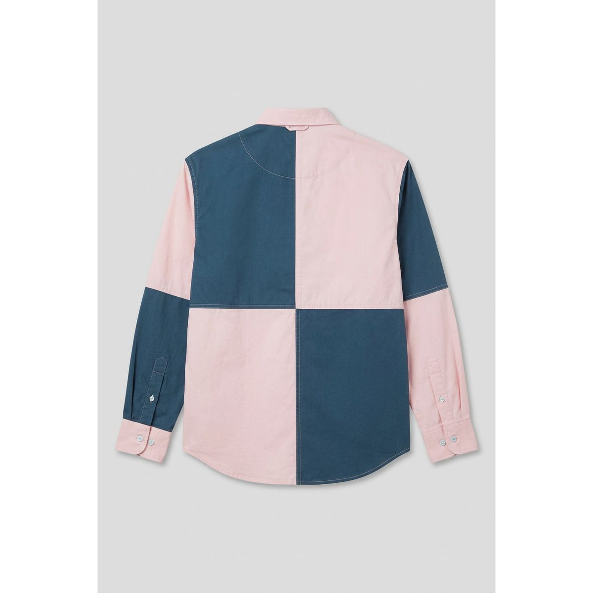 A long-sleeve color-block shirt with a large checkered pattern in teal blue and light pink, shown hanging on a wooden door.