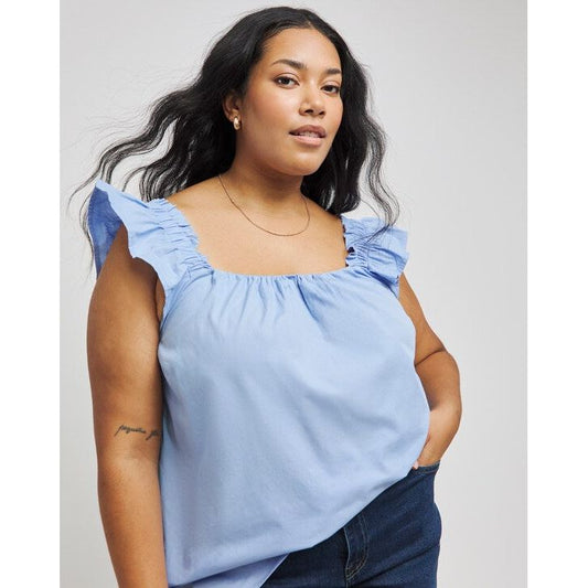 Woman wearing a light blue top with ruffled shoulders against a plain background