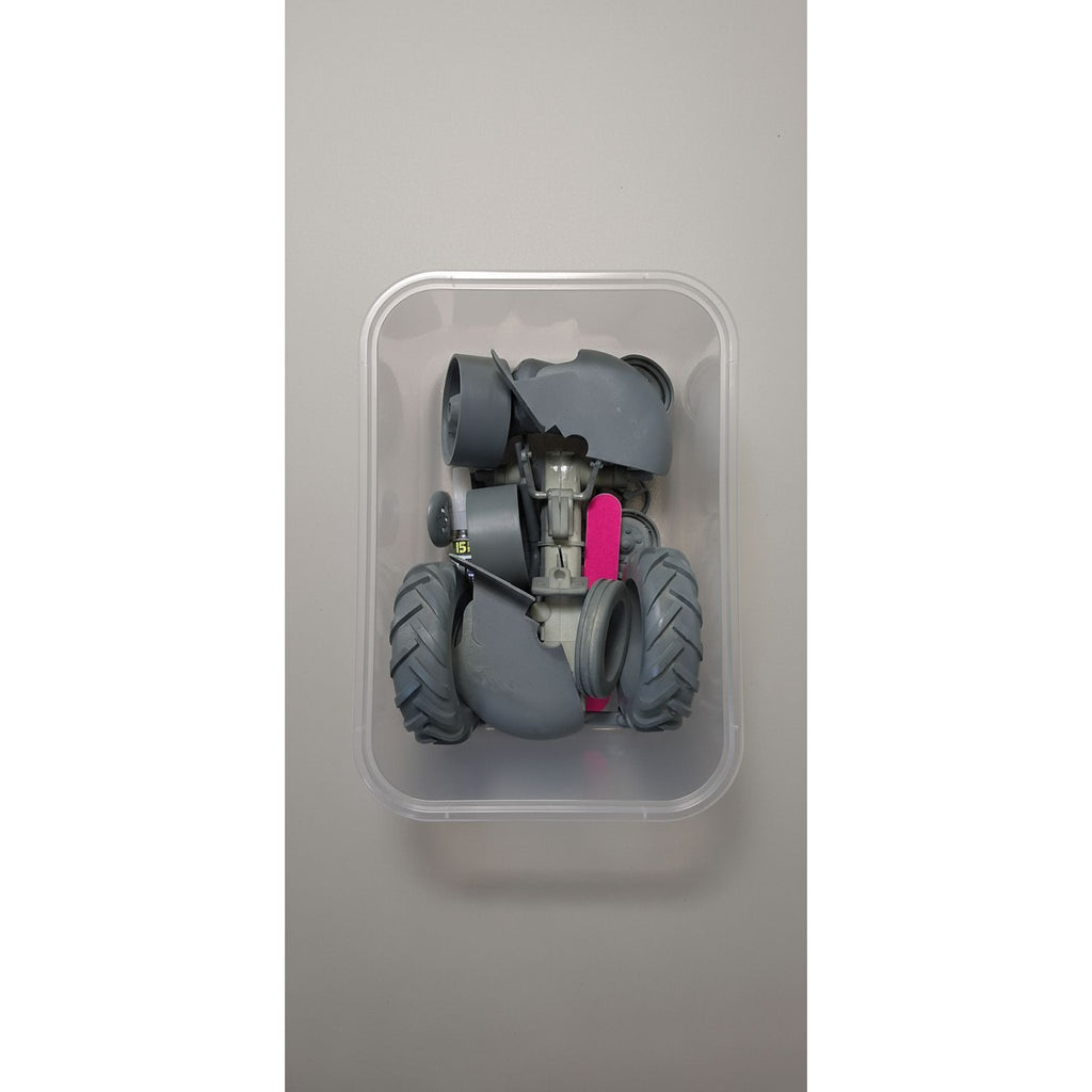 Toy robot with large wheels and a pink component inside a transparent container on a beige surface.